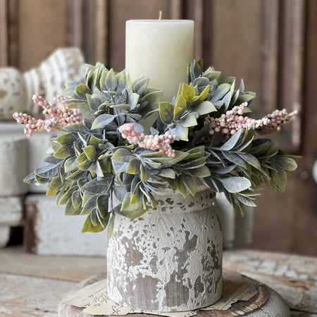 Decorative candle holder with greenery and a candle on a wooden surface.