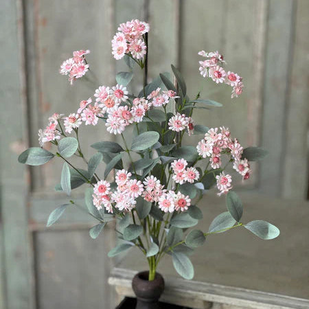 Pink artificial flowers in a decorative pot on a wooden surface